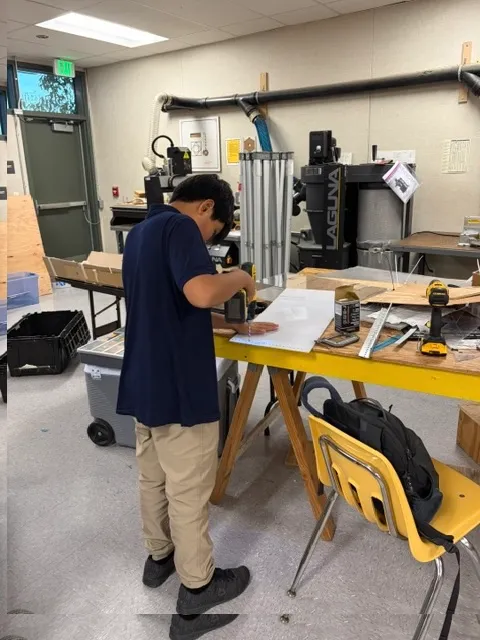 A student using a drill at a workshop workbench.