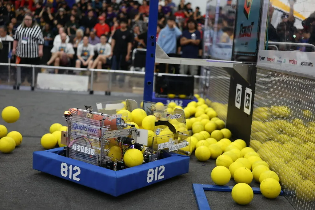 Team 812's competition robot collecting yellow game pieces beside the field wall.